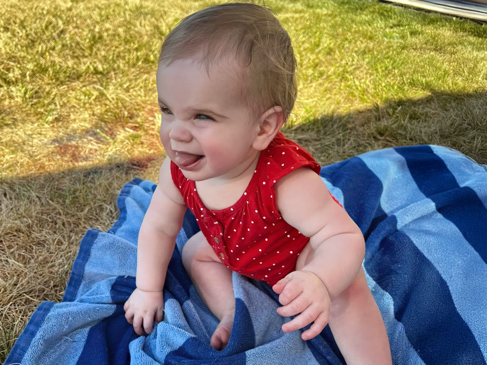 A baby girl in a red dress sits on a blue and white striped blanket, radiating innocence.