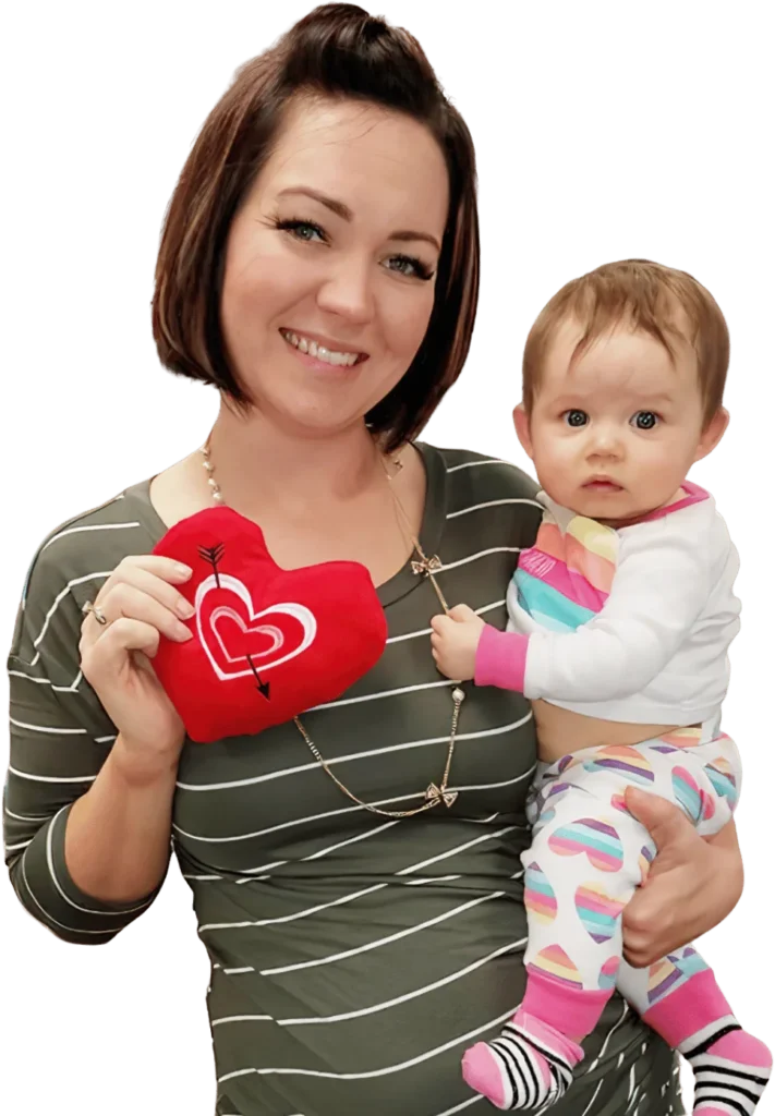 A smiling woman holding a baby girl and a red heart-shaped pillow