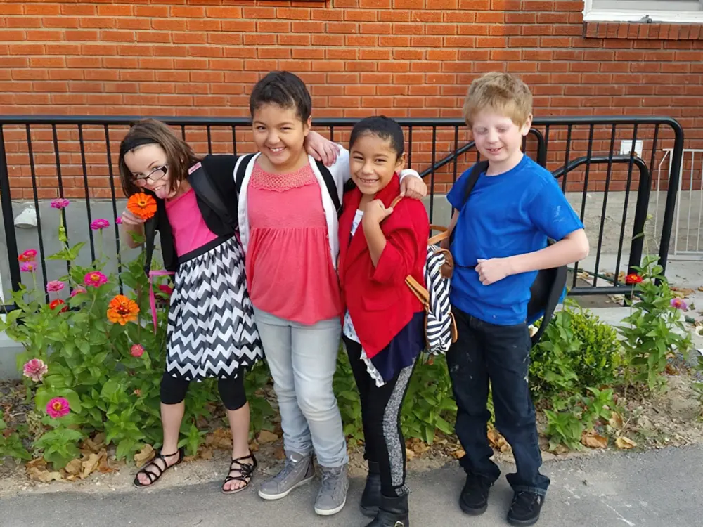 Four school-age children with their arms around each other outside a brick building