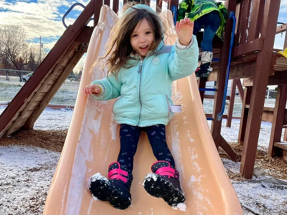 A smiling girl in a mint jacket sliding down a snowy slide