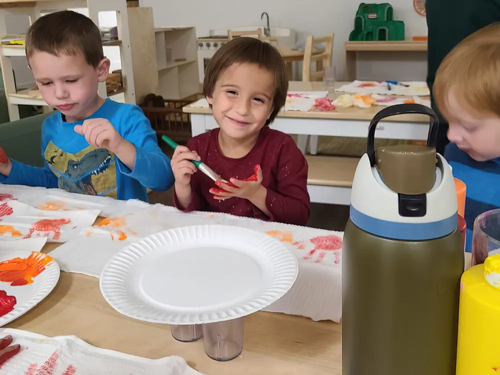 Three children painting at a table covered in paper