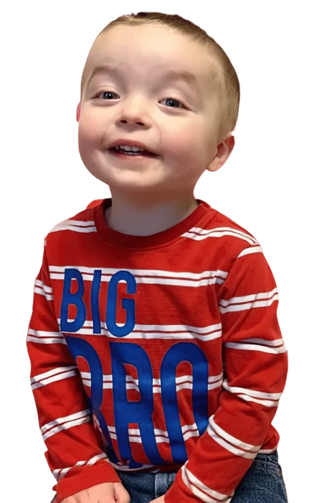 A smiling toddler boy in a red striped “BIG BRO” shirt