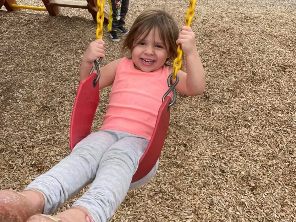 A smiling girl on a playground swing over wood chips