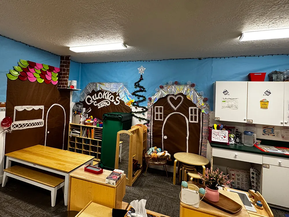 A classroom decorated as a gingerbread village, with a play kitchen and child-size tables