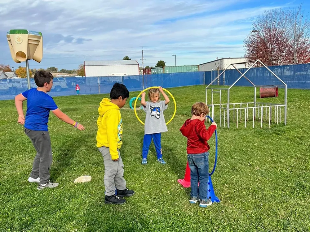 Four children playing with hoops on a fenced, grassy playground