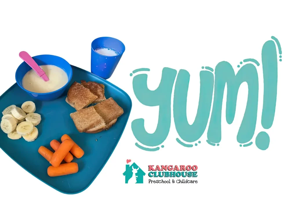 A breakfast tray of cereal, toast, banana slices, carrots and milk beside a hand-lettered “Yum!” and the Kangaroo Clubhouse logo