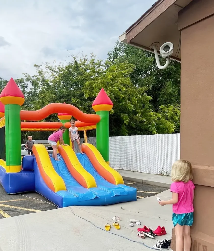 Children playing on an inflatable bounce-house slide outside the center, with a security camera on the wall above them