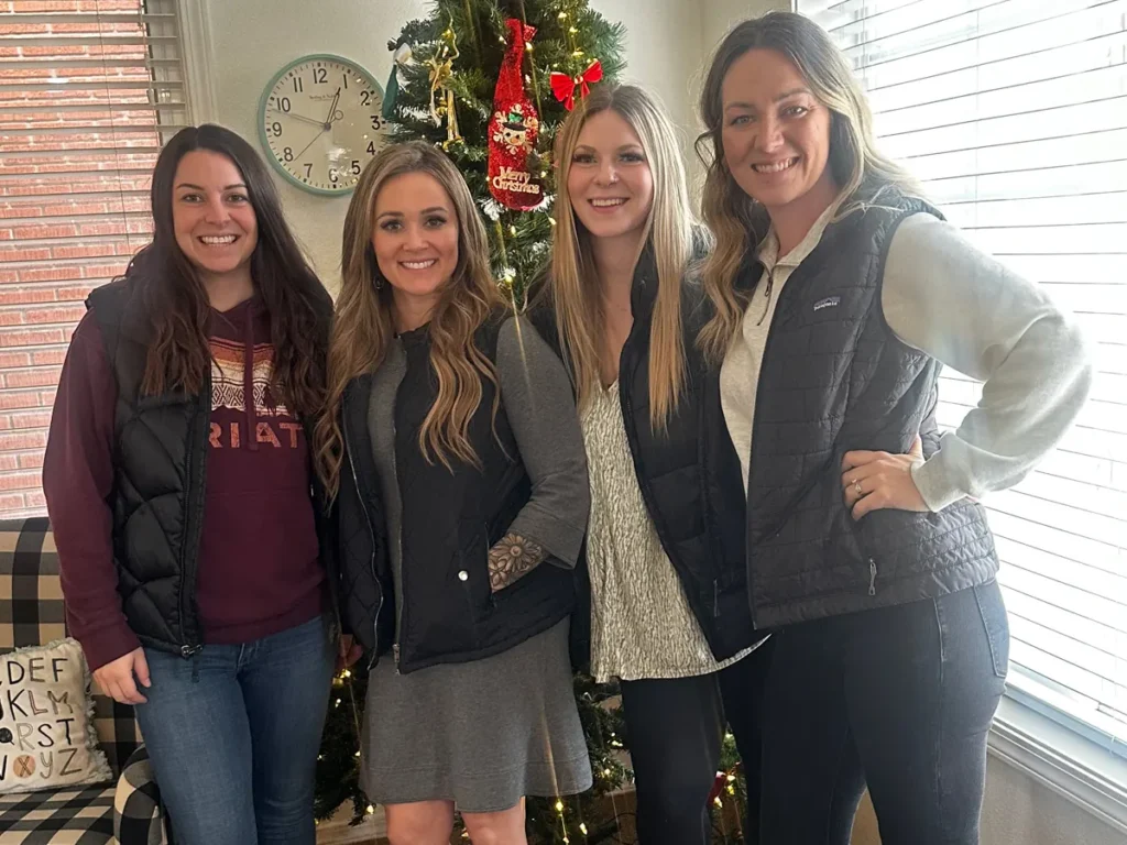 Four smiling Kangaroo Clubhouse team members standing together in front of a decorated Christmas tree