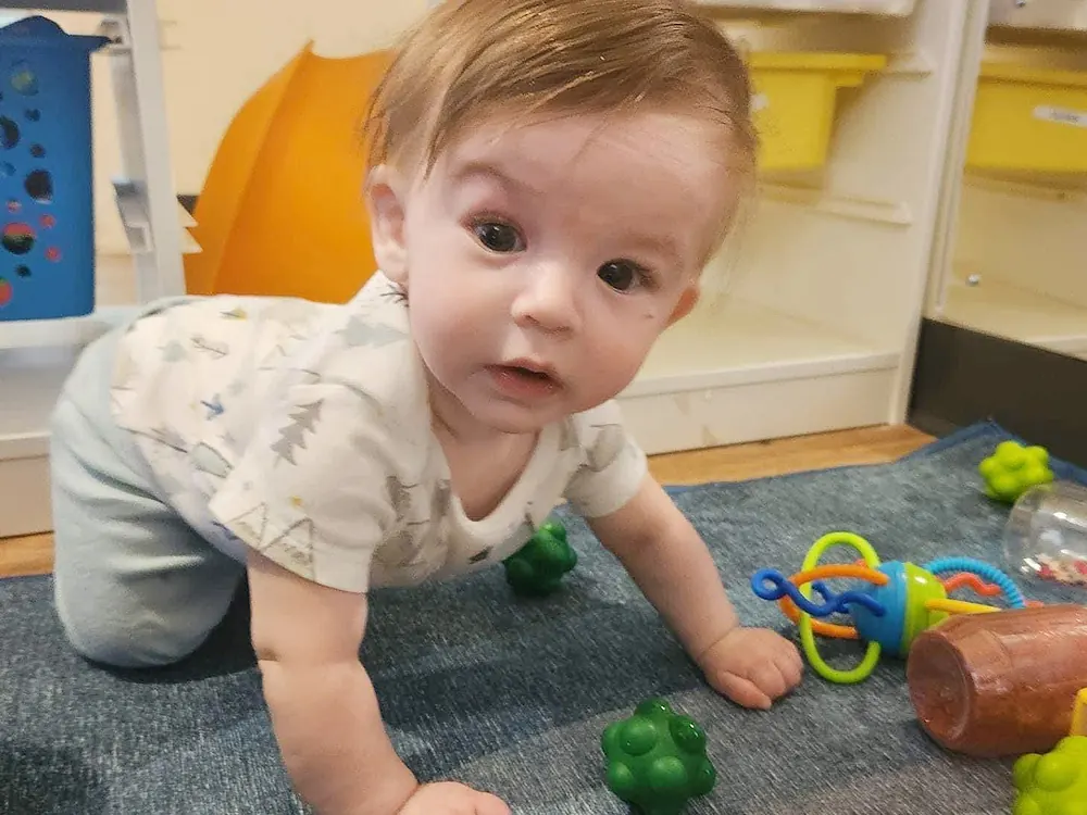 A baby crawling across a playroom rug among toys