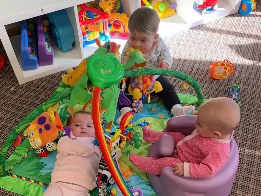 Three babies playing on an activity mat and in a baby seat among colorful toys