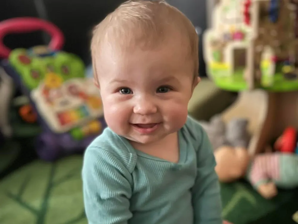 A smiling baby in a teal shirt among the toys