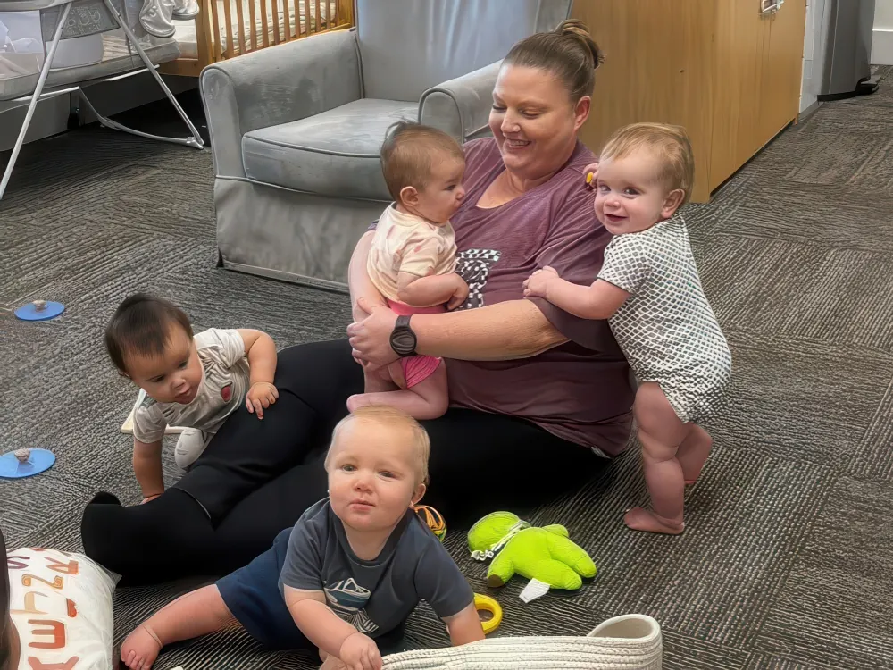 A teacher sitting on the carpet surrounded by four babies