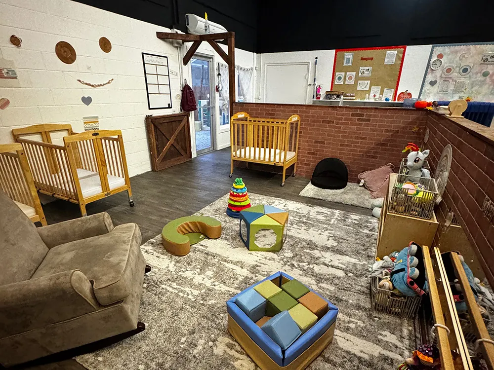 An infant room with cribs, a sofa and a soft play cube on a patterned rug