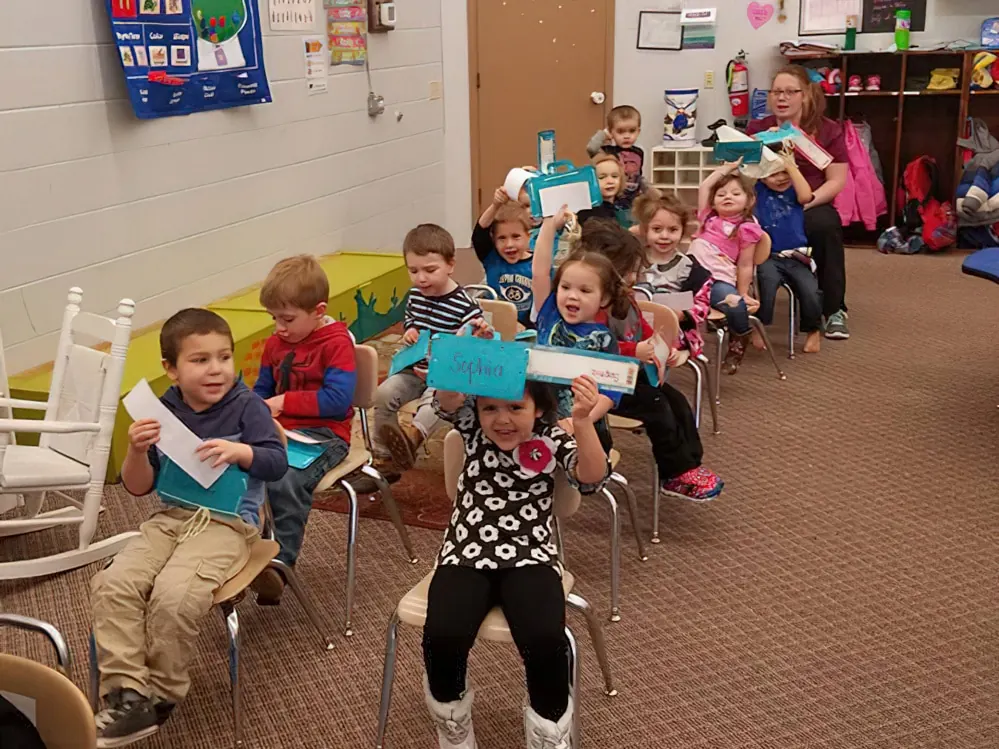 A classroom of children sitting on chairs and holding up paper cards