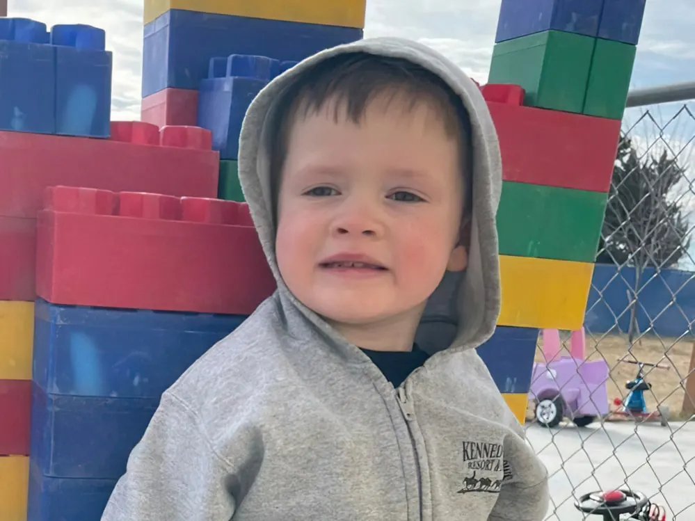 A boy in a gray hoodie in front of a wall of giant toy building blocks