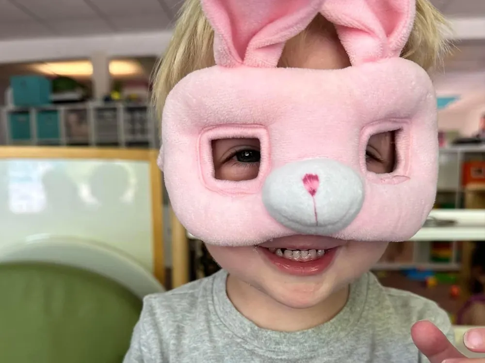 A grinning toddler wearing a pink bunny mask