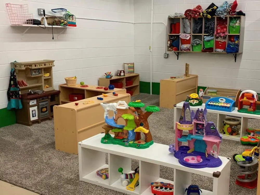 A tidy toddler classroom with toy shelves, a play kitchen and dollhouses