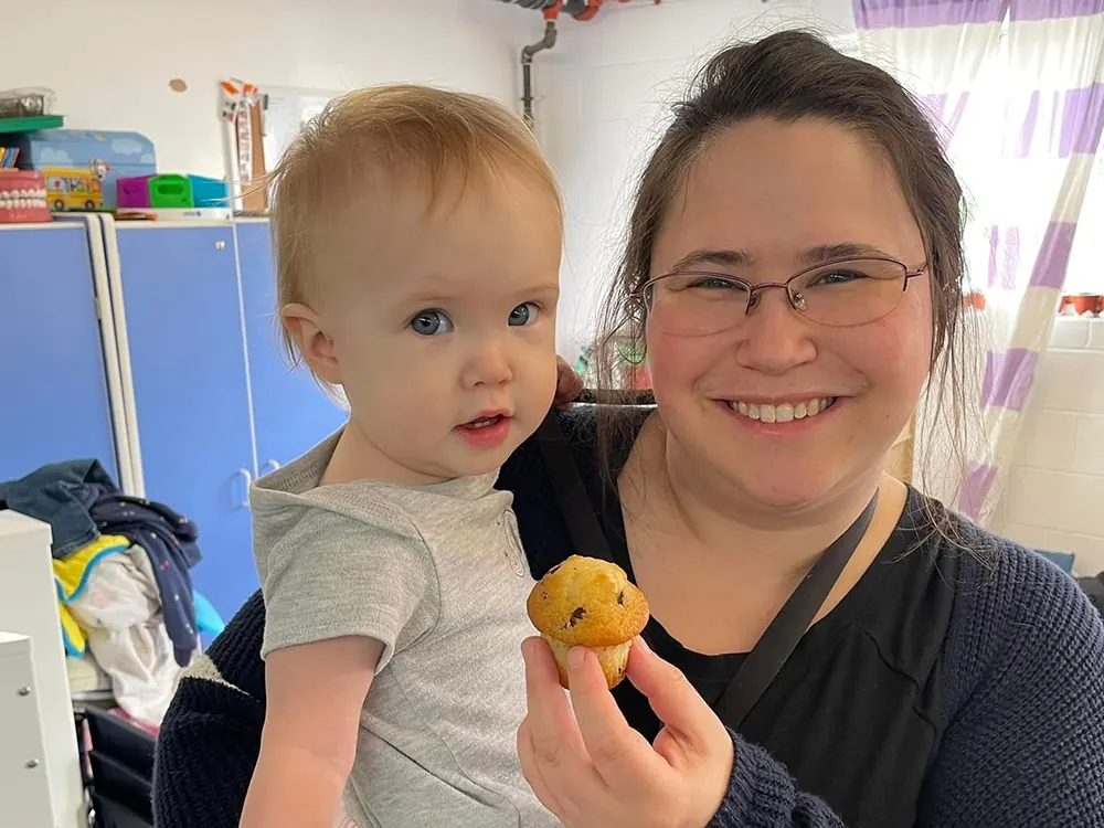 A smiling woman holding a baby boy who holds a muffin