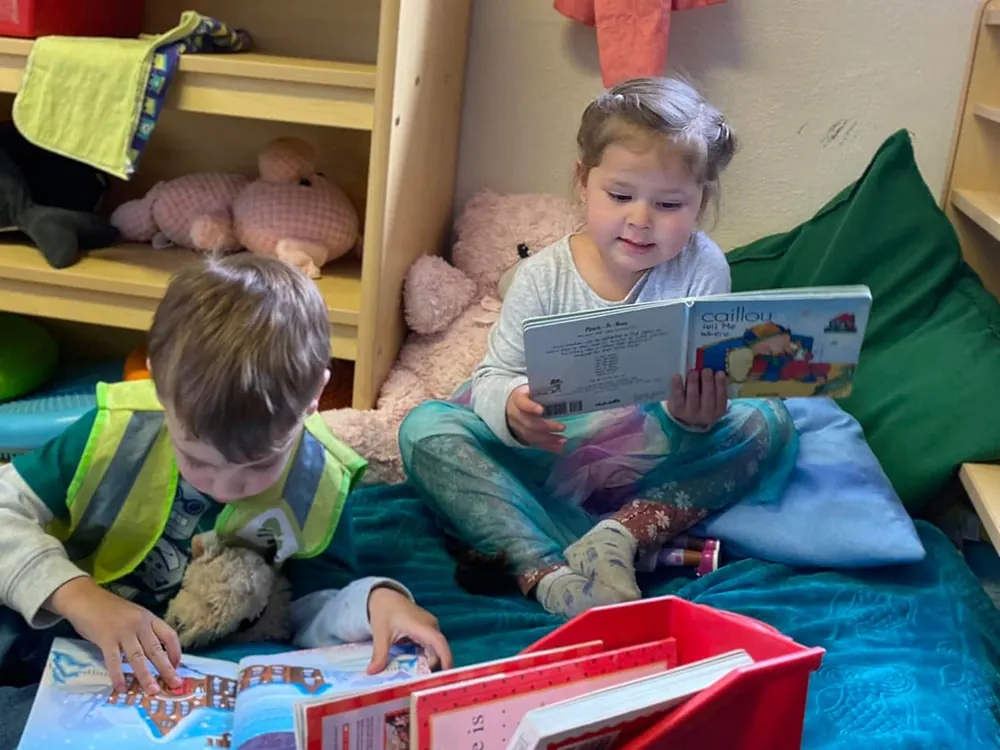 Two toddlers reading picture books on a cushion in a reading nook